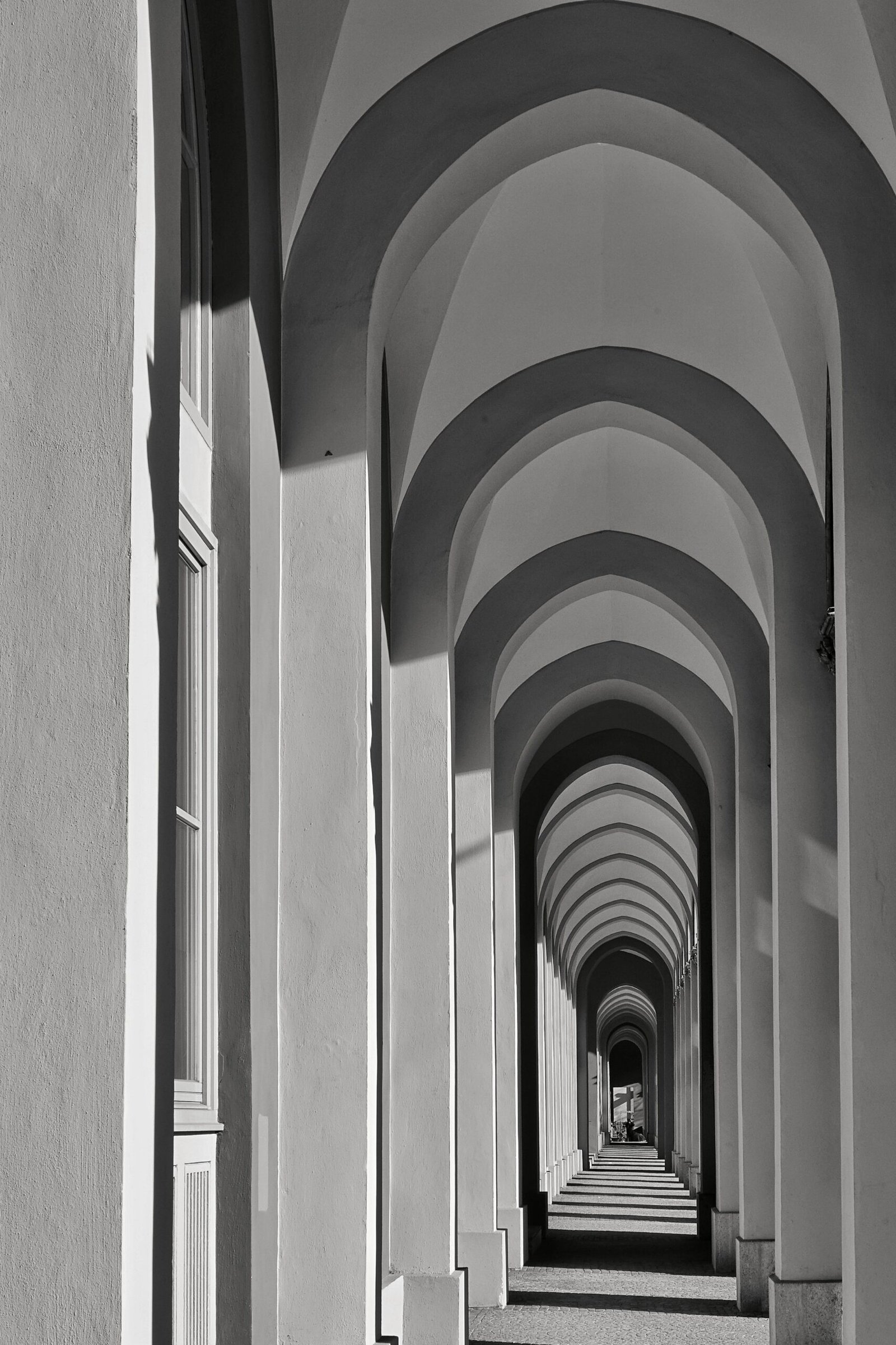 vertical grayscale shot of a long corridor with multiple arch shaped columns
